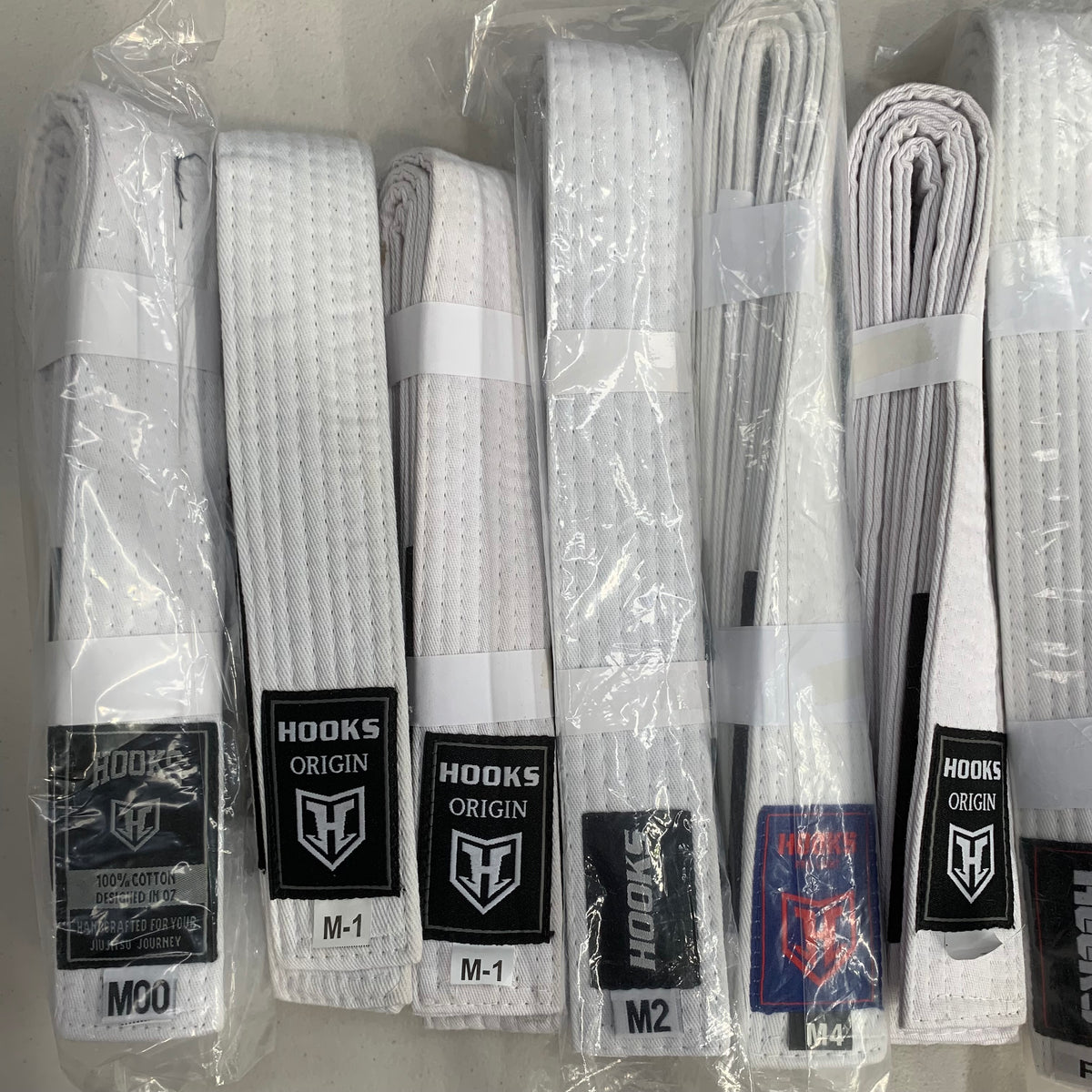 Hooks Clearance White BJJ Belt, multiple belts in packaging showing various sizes from M00 to M4