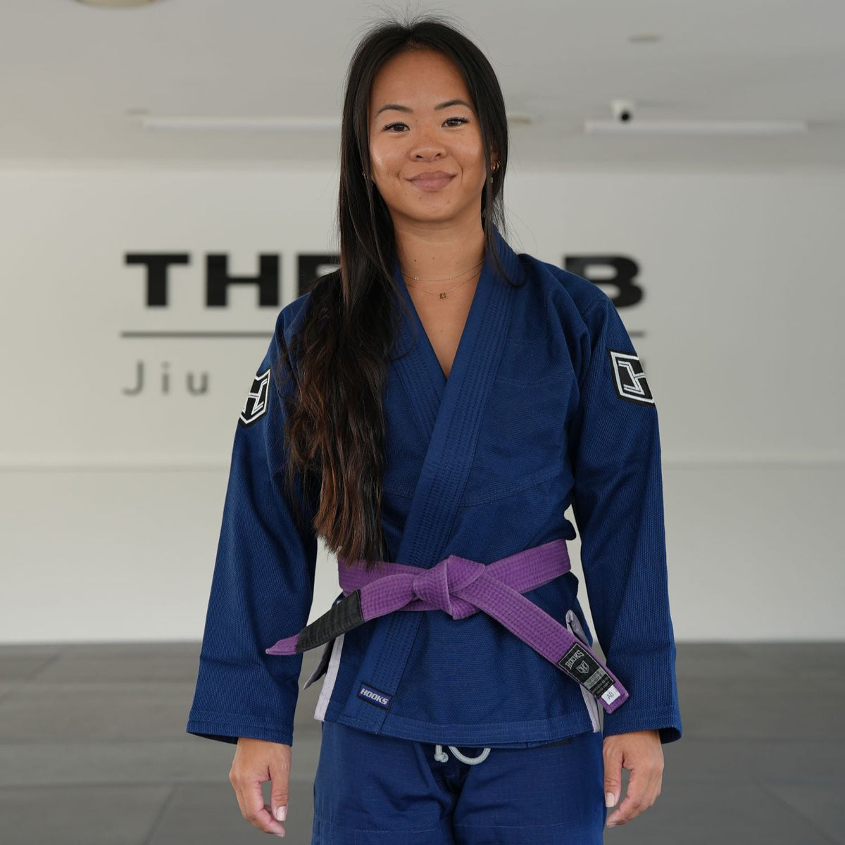 Hooks BJJ Gi Prolight II Navy, front view worn by a person, shown with a purple belt in a gym setting
