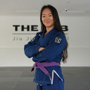 Hooks BJJ GI Prolight II Navy, worn front view with purple belt, arms crossed, inside a BJJ academy