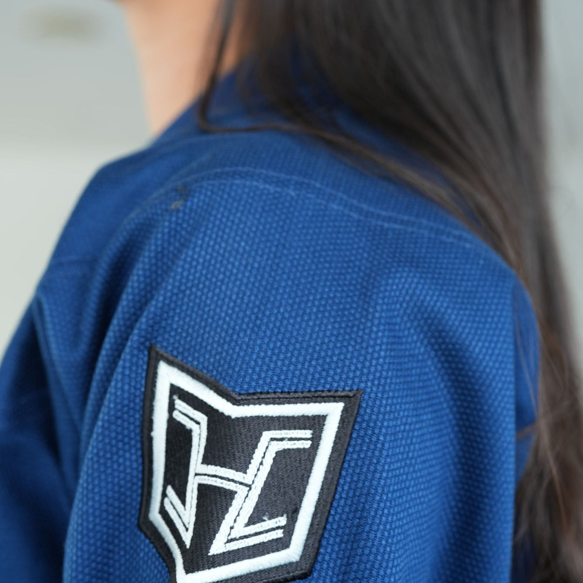 Hooks BJJ GI Prolight II Navy, close-up of embroidered sleeve patch, worn by a person