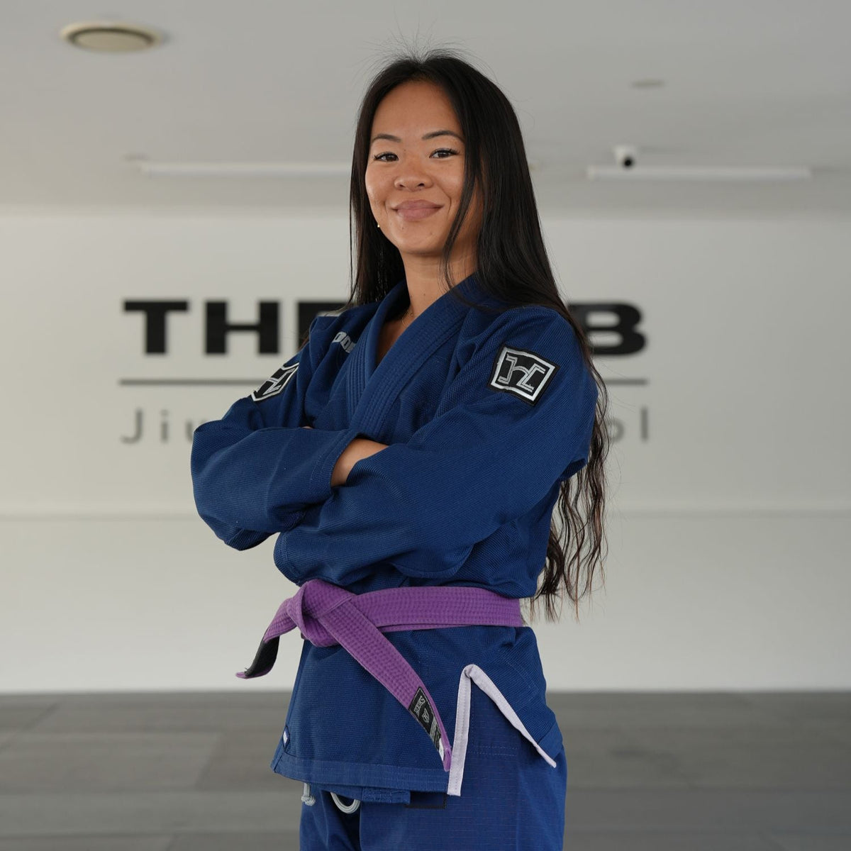 Hooks BJJ GI Prolight II Navy, worn front view with purple belt, arms crossed, showing shoulder patch detail