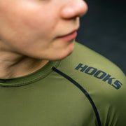 Hooks short sleeve rashguard close-up showing chest logo and black contrast shoulder seam, worn by a person