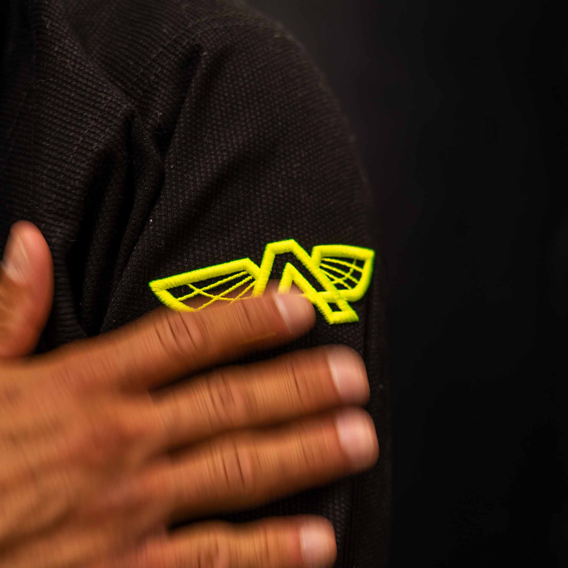 Close-up of the yellow embroidered logo on The Atlas Brand ICON Black rashguard.